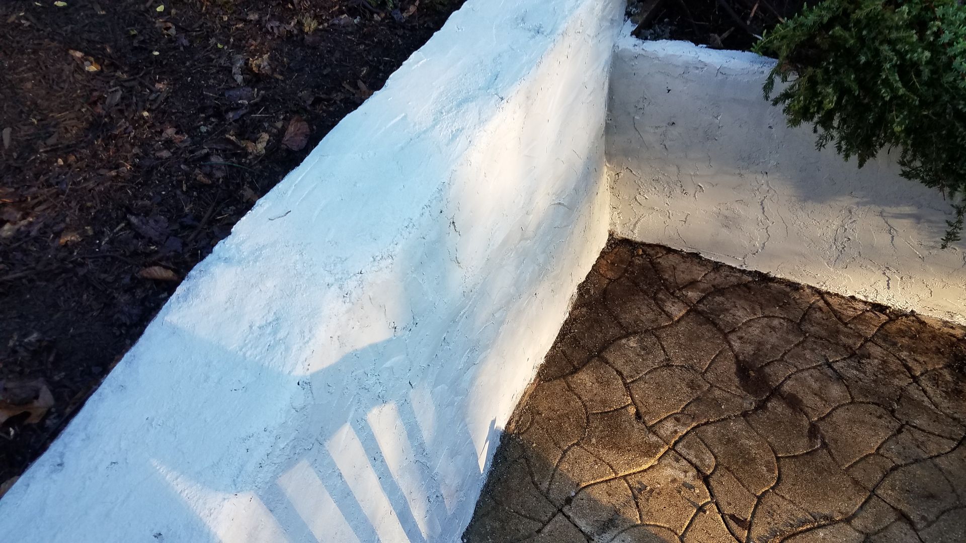 A white wall is sitting next to a brick walkway.