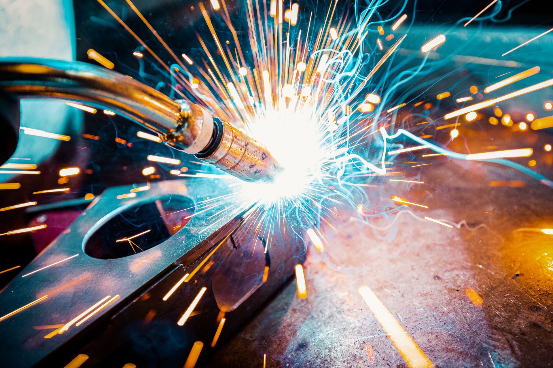 A close up of a person welding a piece of metal with sparks coming out of it.
