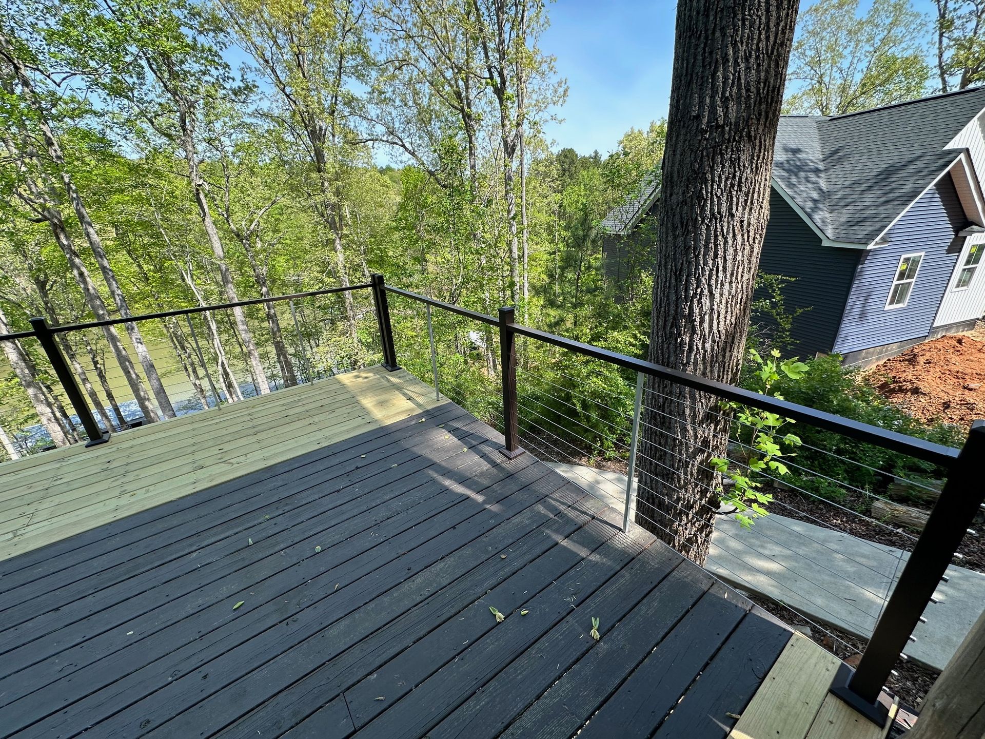 A black deck with a glass railing and trees in the background.