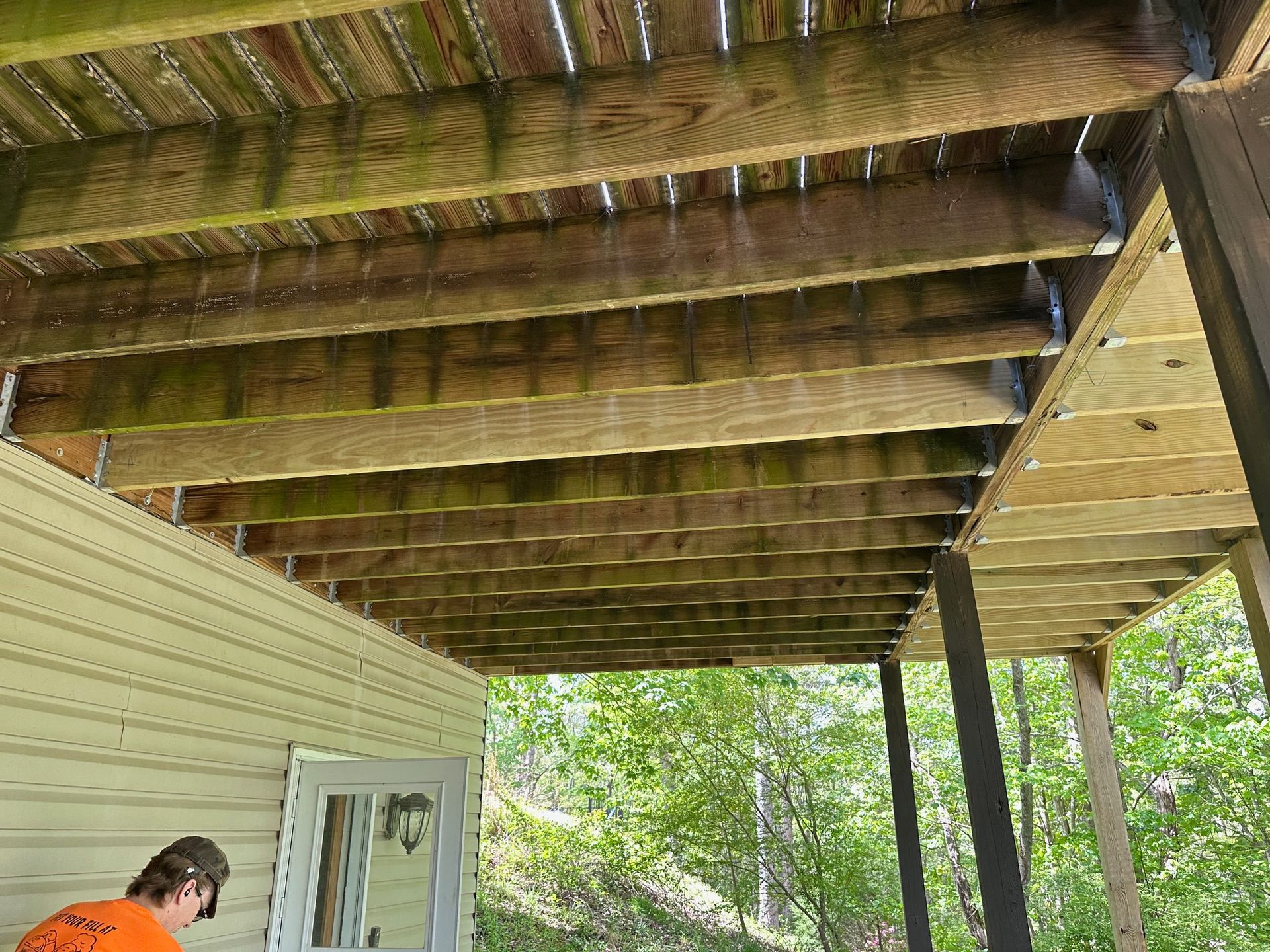 A man is standing under a wooden deck next to a house.