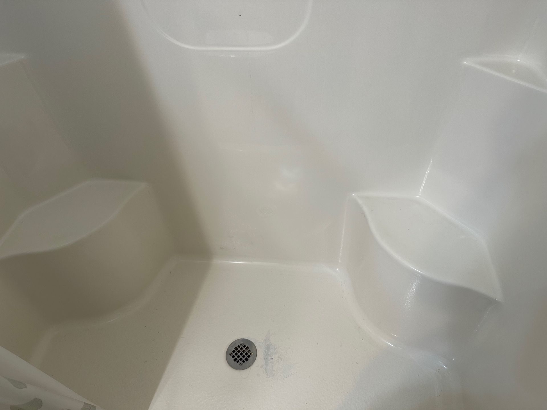 A white shower stall with a drain and shelves.