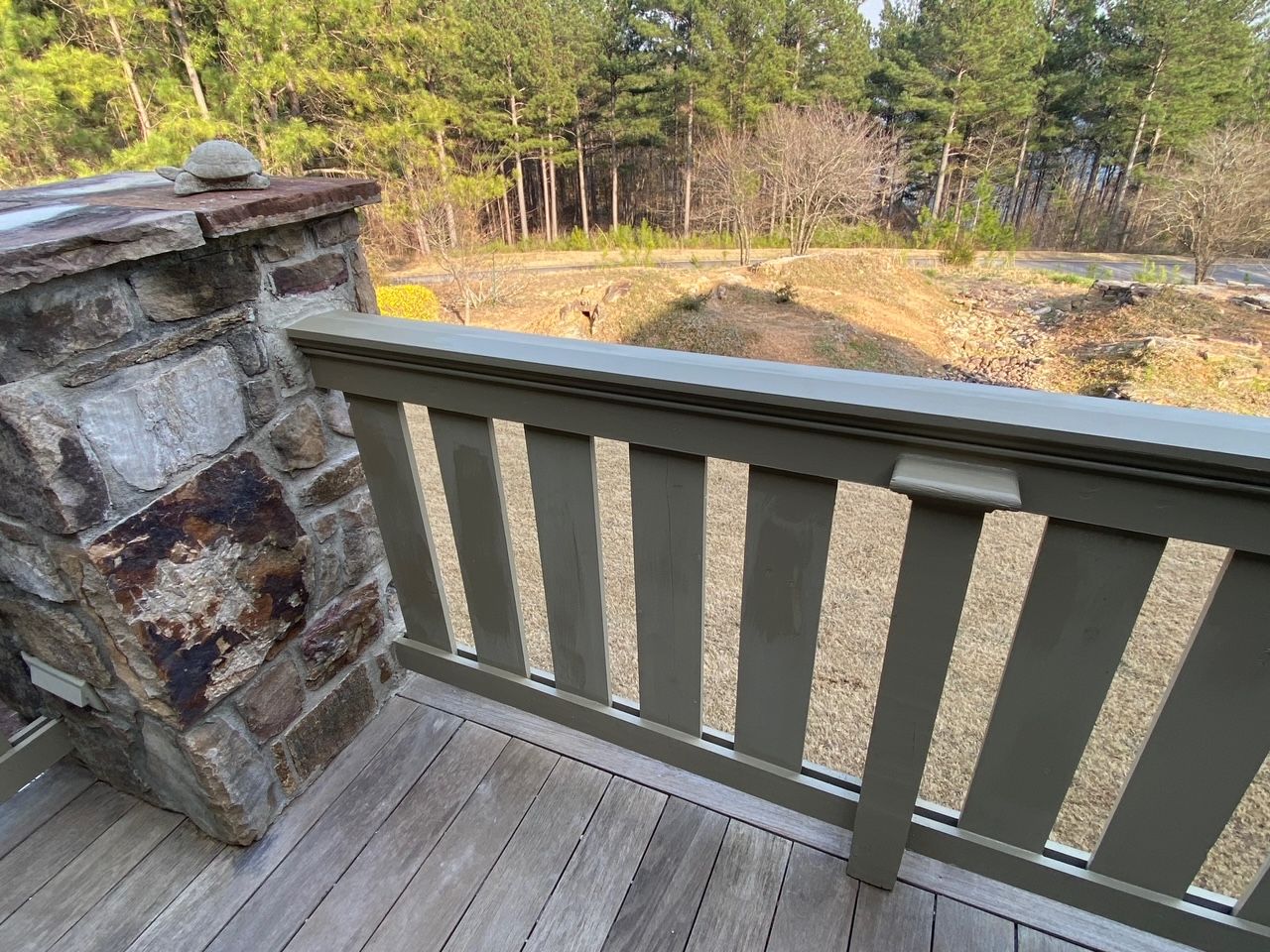 A wooden railing on a deck with a view of a forest.