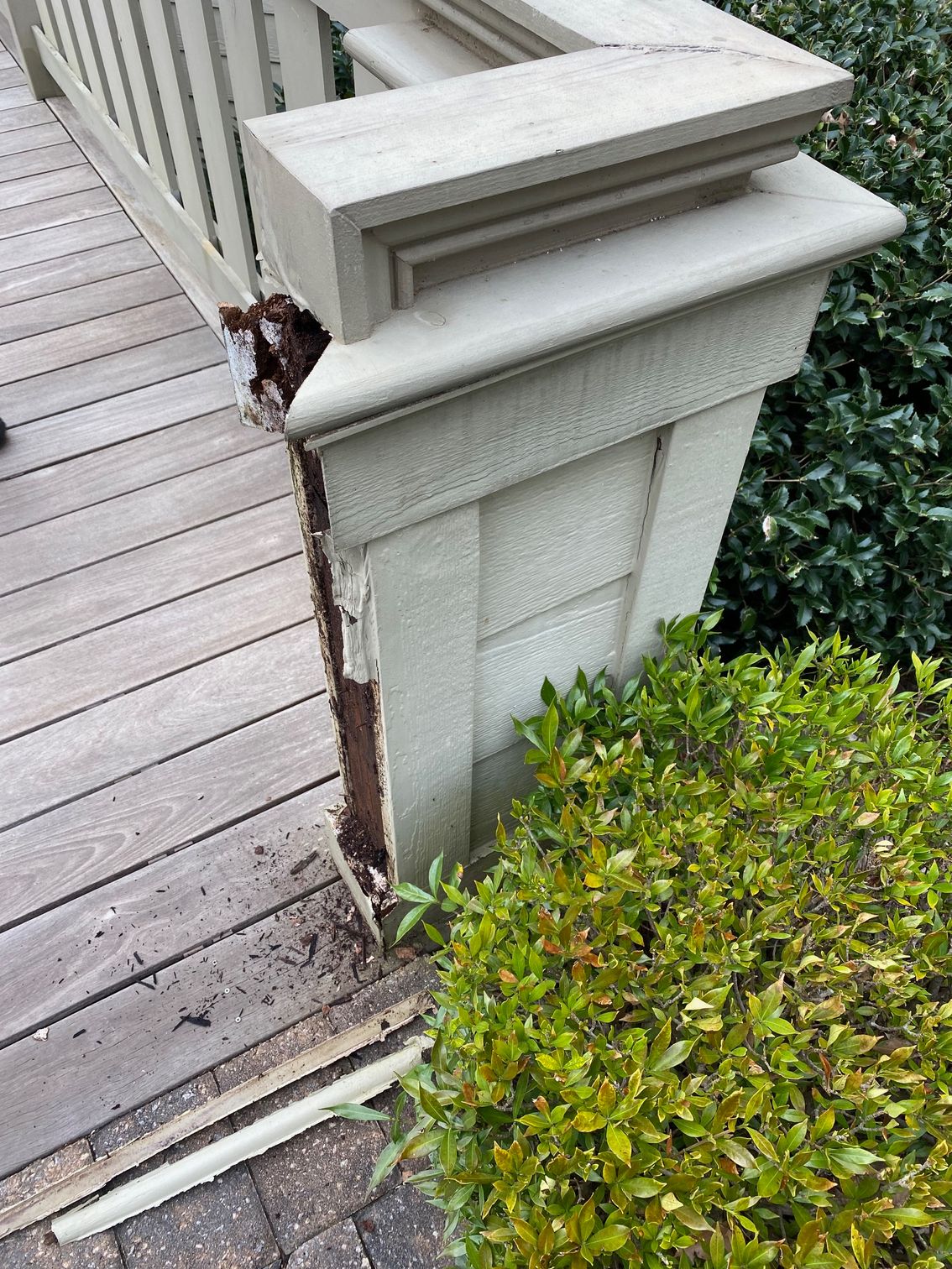 A wooden deck with a broken railing next to a bush.