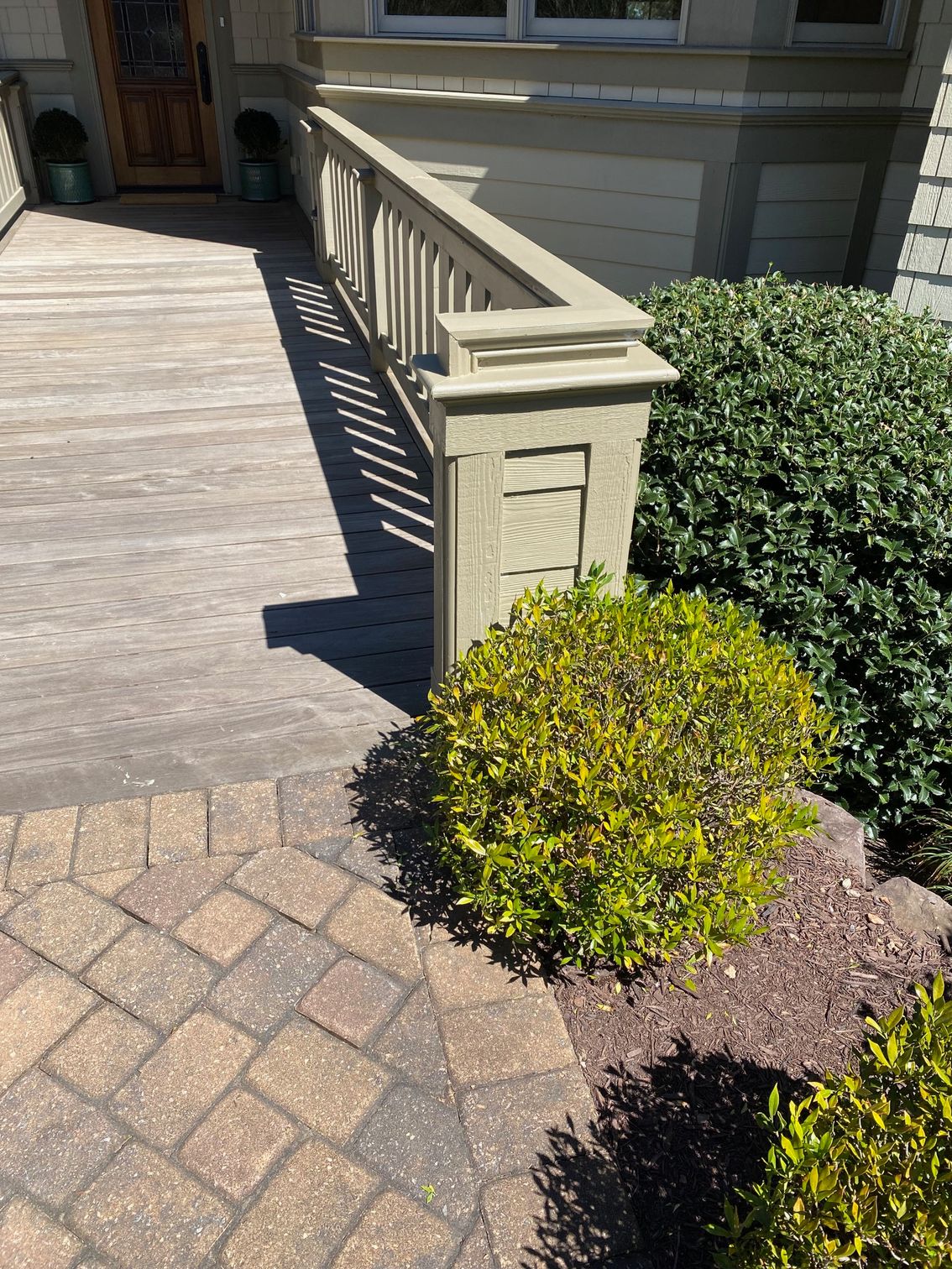 A wooden deck with a railing and a brick walkway in front of a house.