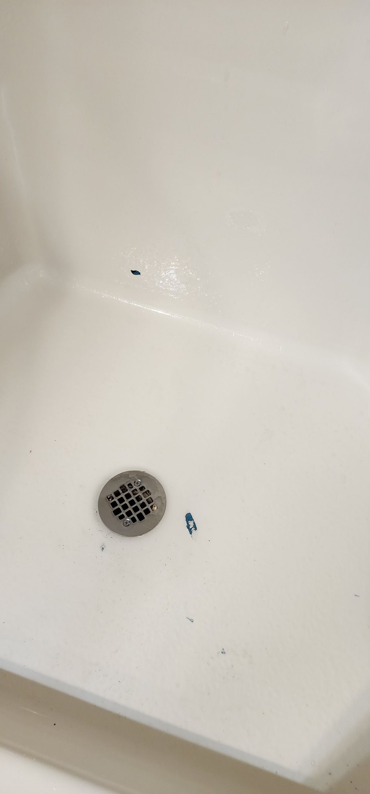 A white shower stall with a drain and a hole in the wall.