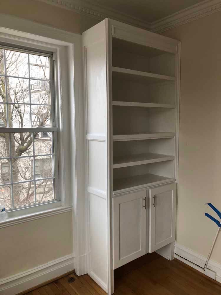 A white bookshelf is in a room next to a window.