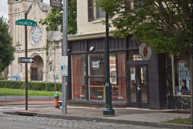 Street corner with a storefront café, church sign, and cobblestone sidewalk under trees.