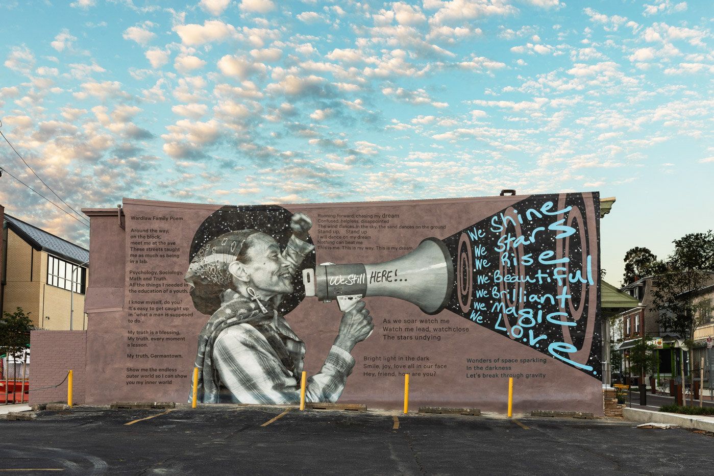 Mural of a child speaking into a megaphone on a brick wall, with blue script and a cloudy sky above.