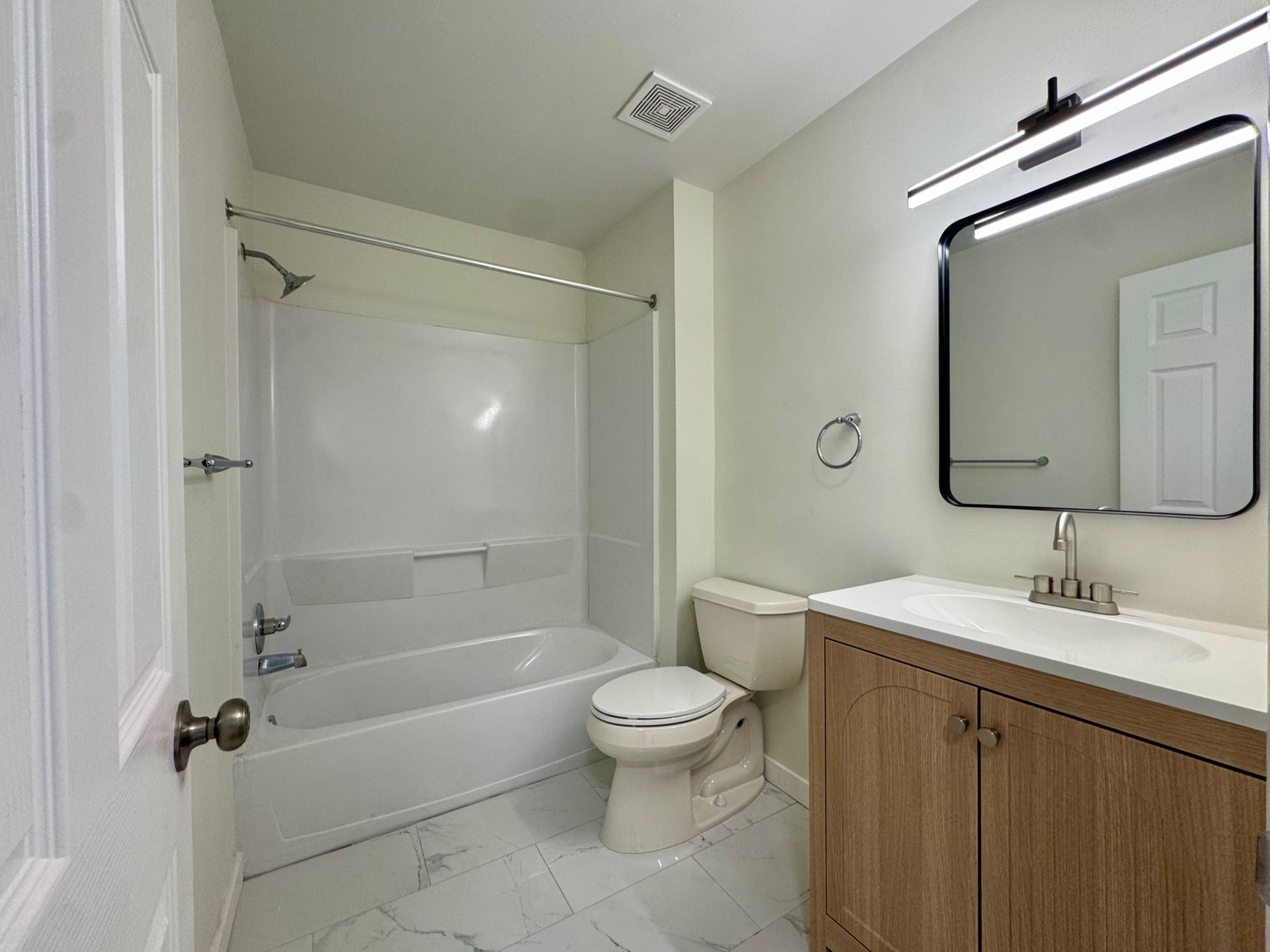 Bright bathroom with white tub, toilet, and wooden vanity with mirror.