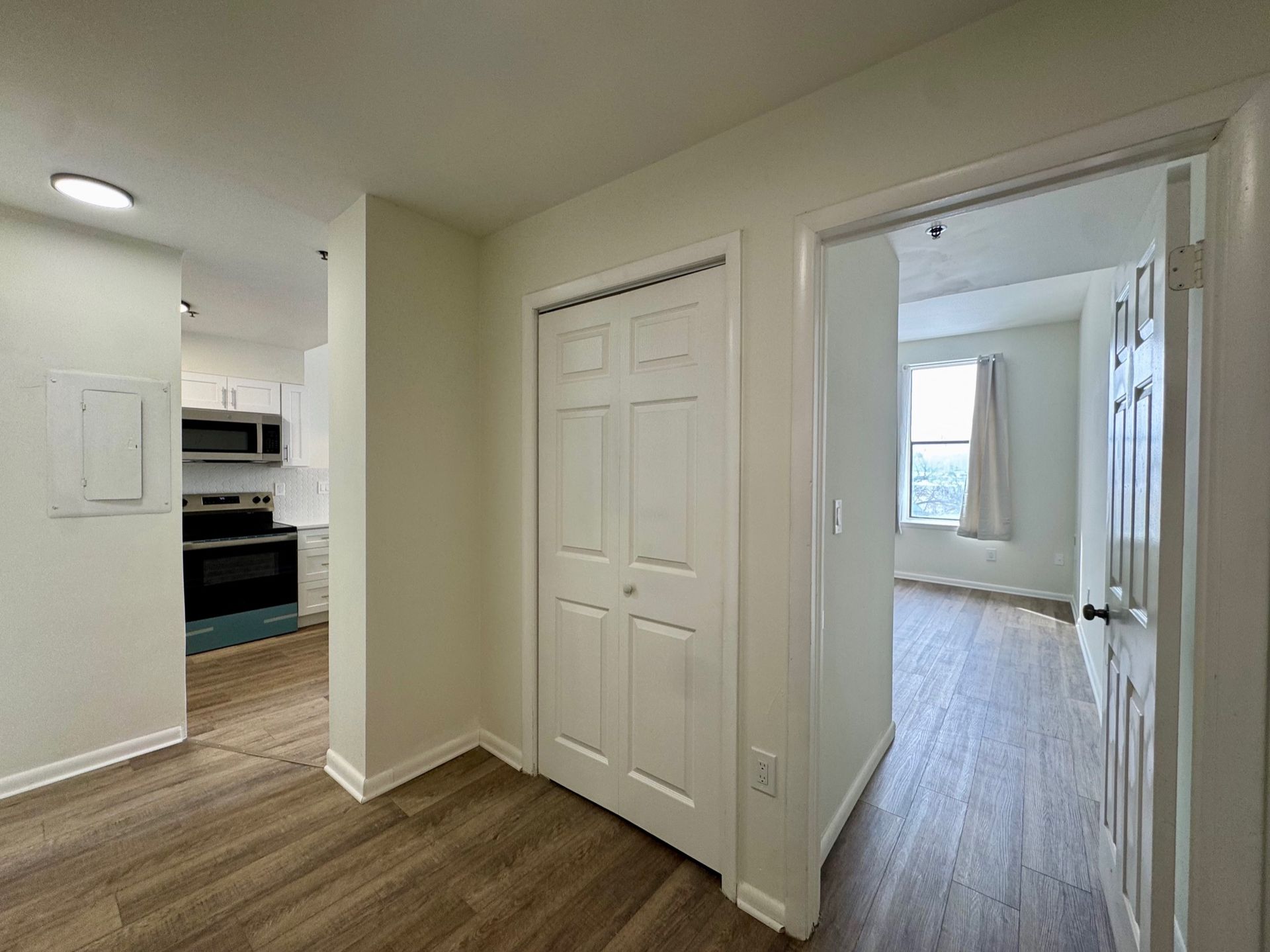 Empty hallway with wood floors, white walls, closets, and a view into the kitchen and bedroom