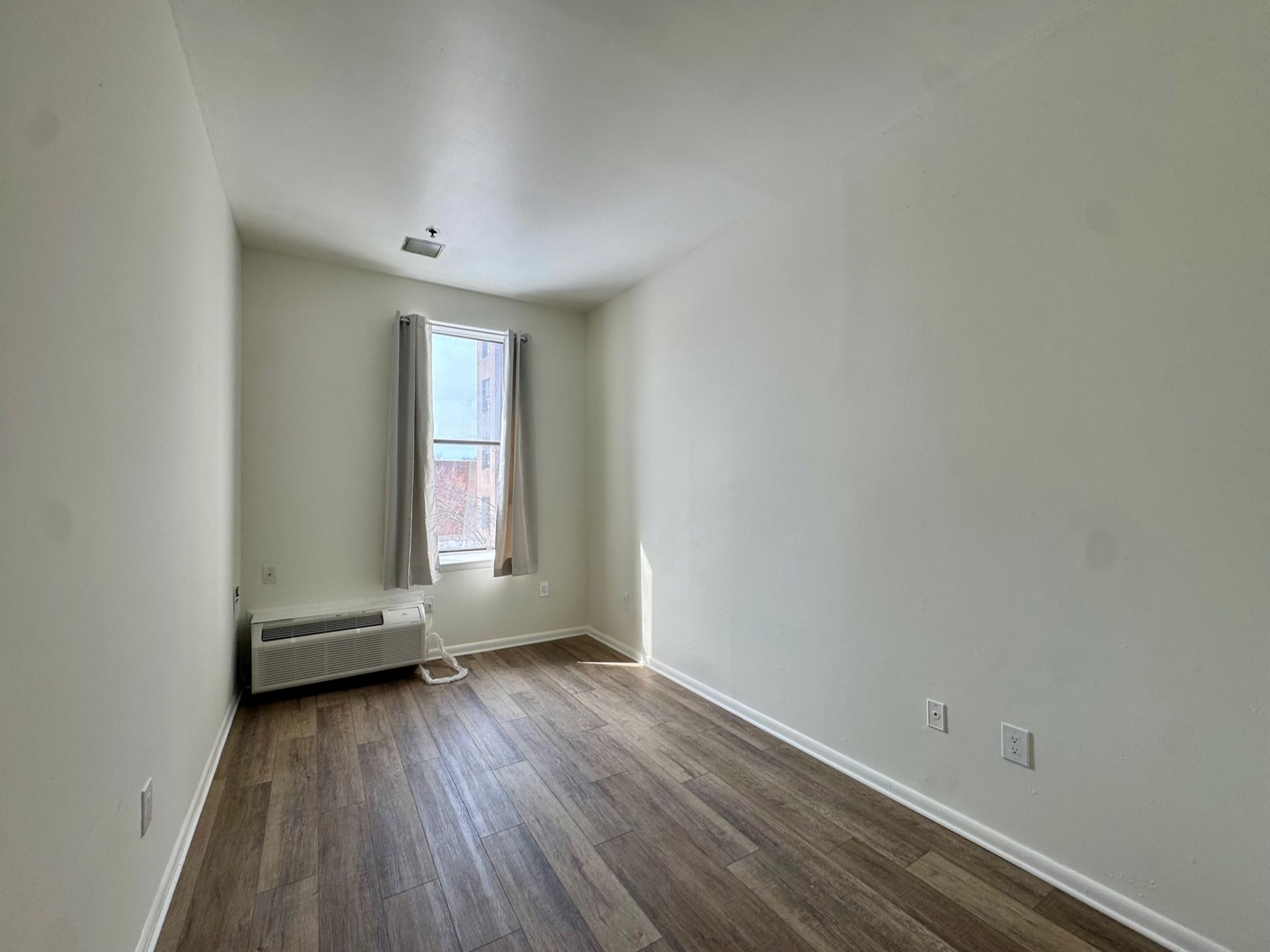 Empty white room with wood floors, a window, and a wall-mounted radiator.
