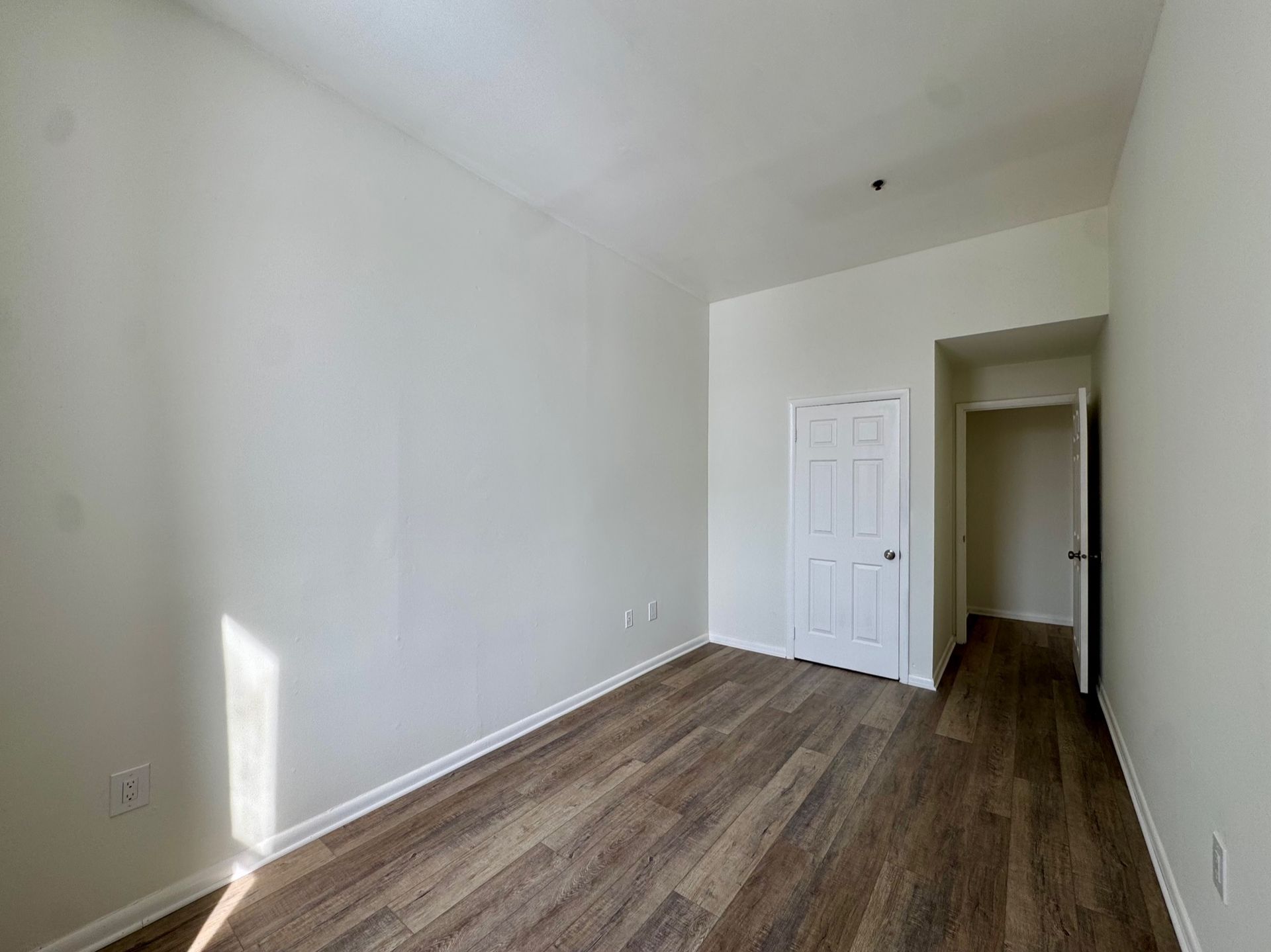 Empty white room with wood-look flooring, a closet door, and hallway opening.