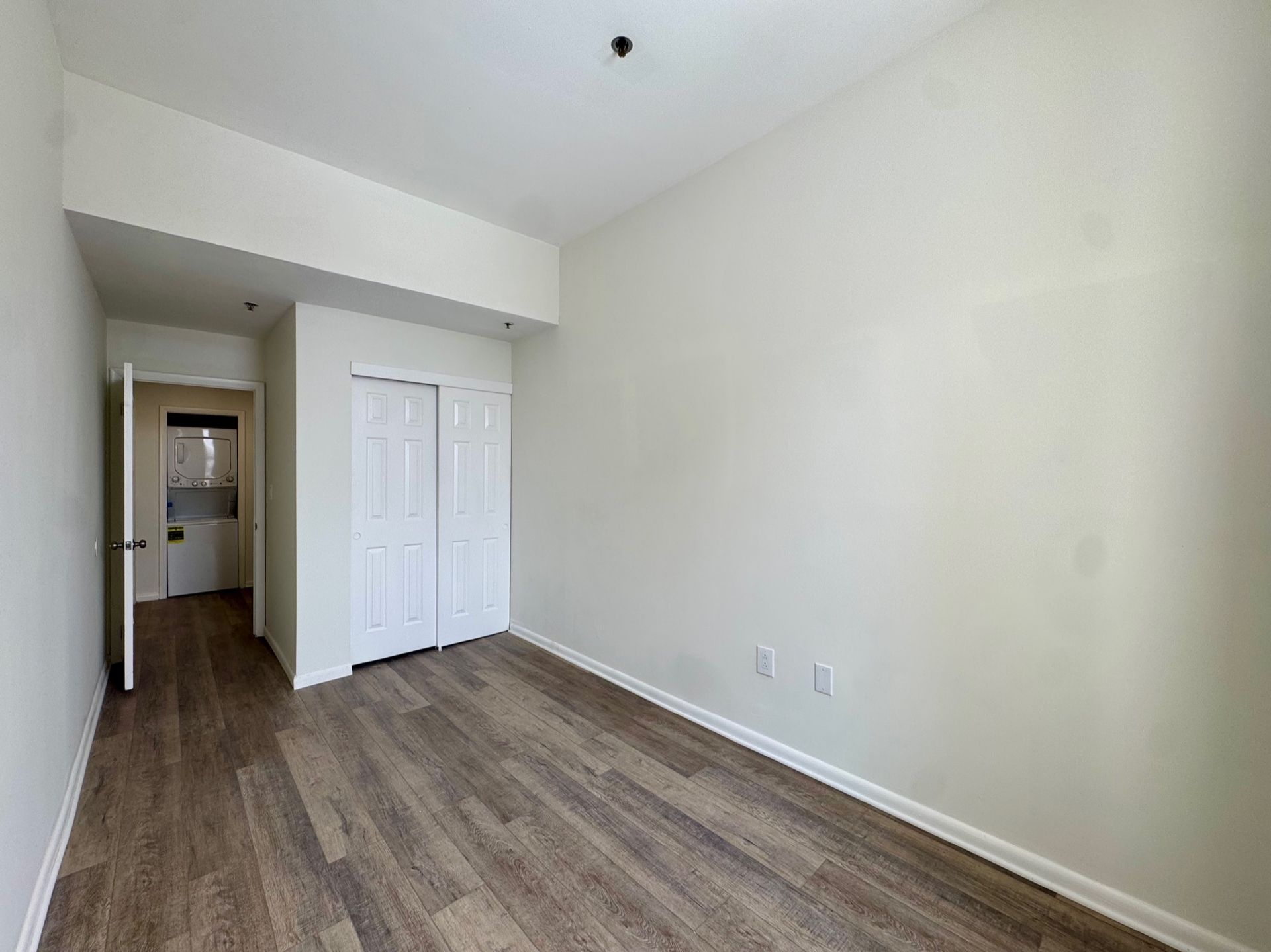 Empty beige bedroom with wood-look flooring and a hallway doorway at the back