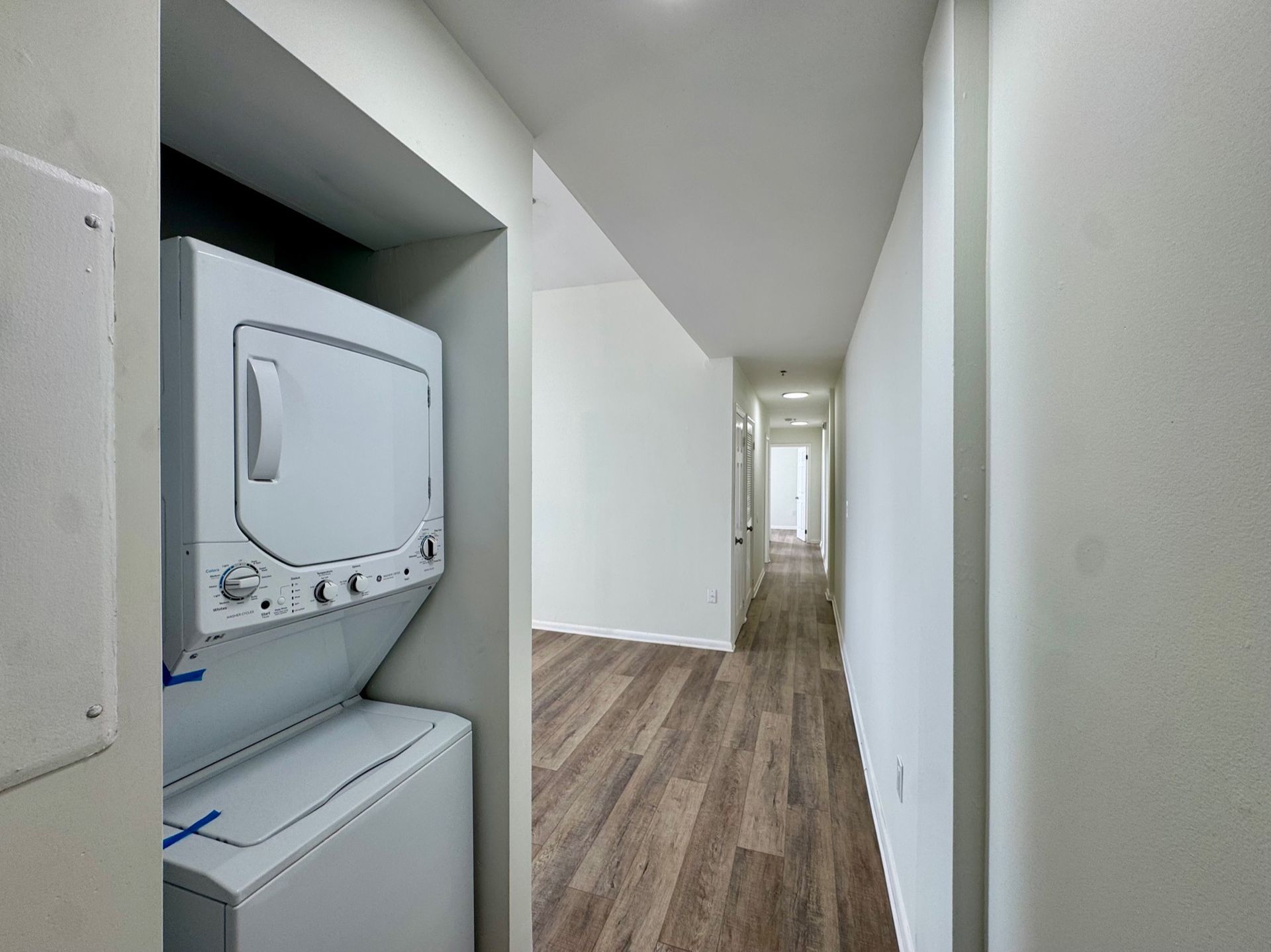 Narrow hallway with wood flooring and a stacked washer-dryer built into a closet on the left.