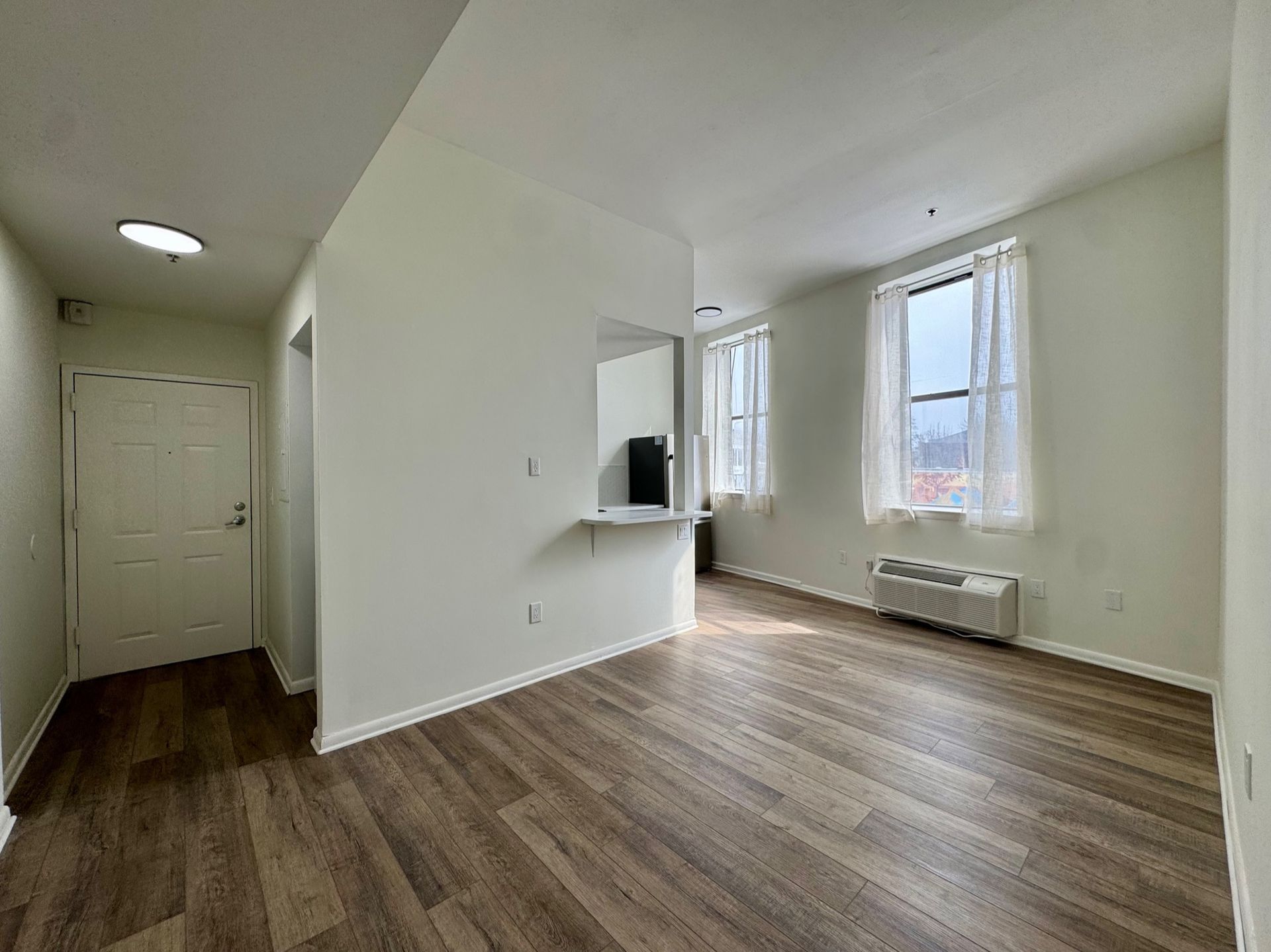 Empty bright living room with wood floors, white walls, and large windows