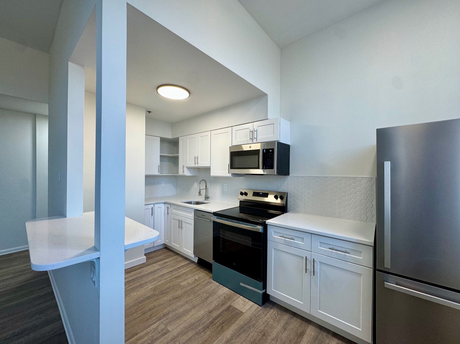 Bright modern kitchen with white cabinets, stainless steel appliances, and light wood flooring