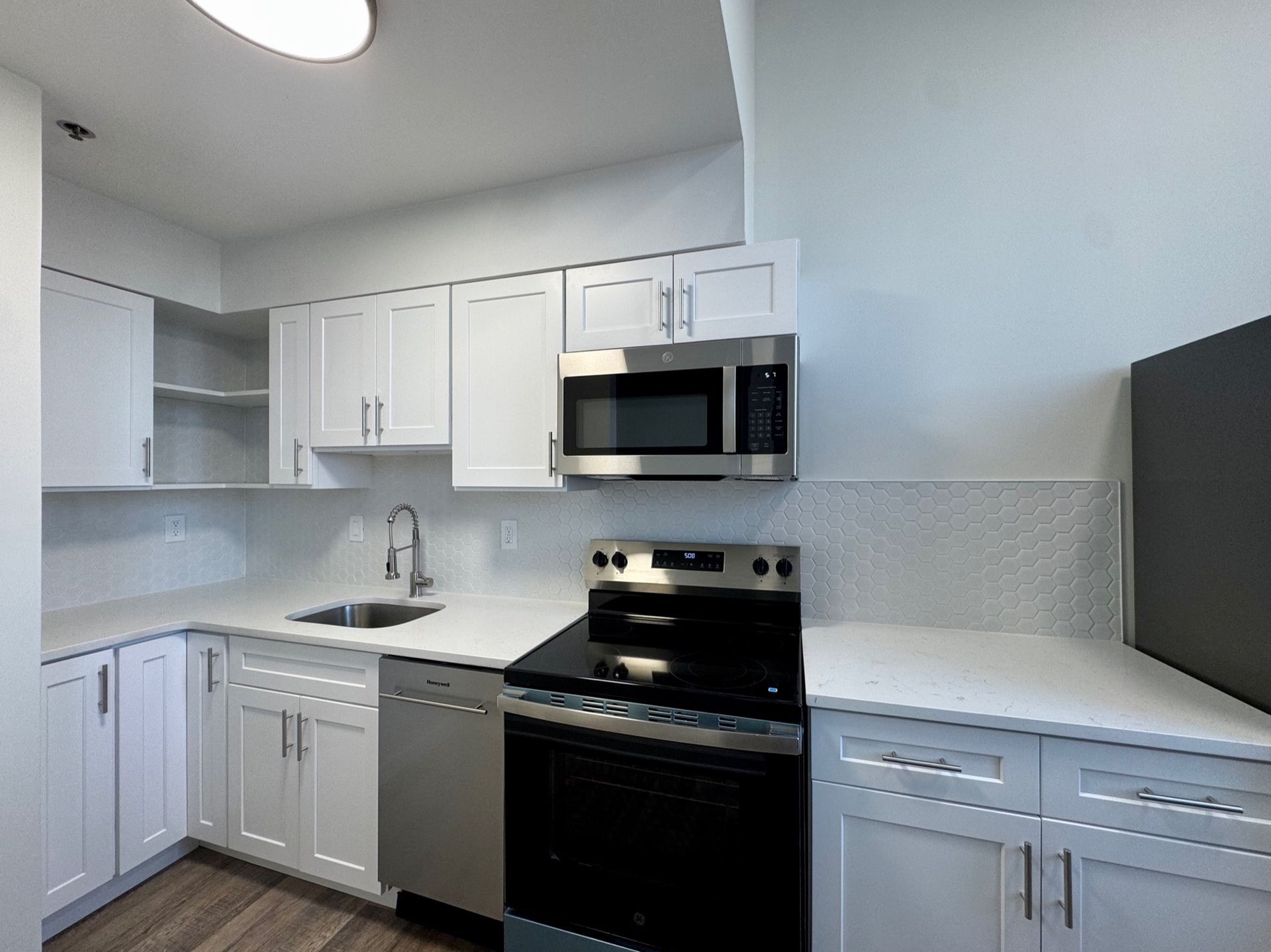 Modern white kitchen with stainless steel appliances, gray backsplash, and light countertops
