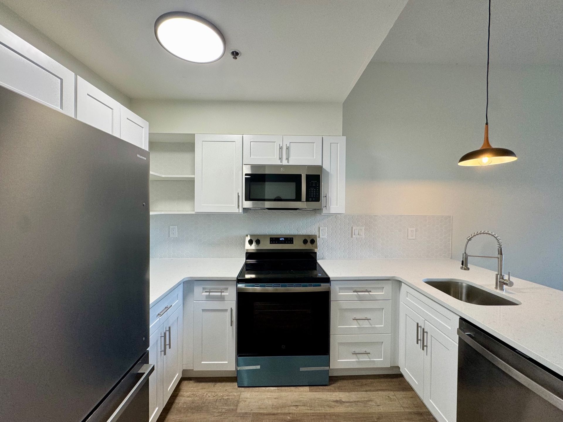 Modern white kitchen with stainless appliances, black stove, and pendant light over a sink.
