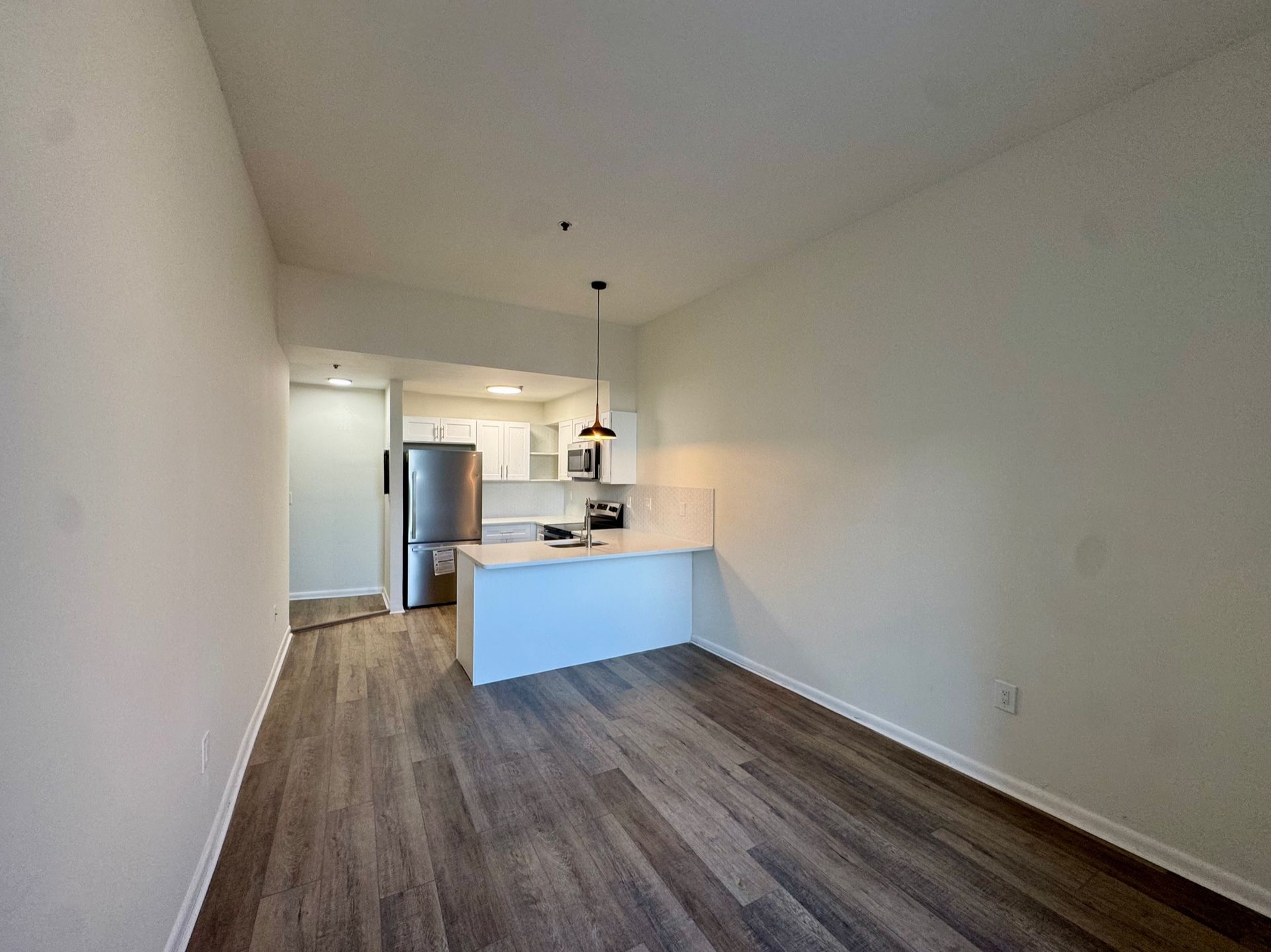 Empty open-plan living room with wood floors and a small kitchen island in a white apartment