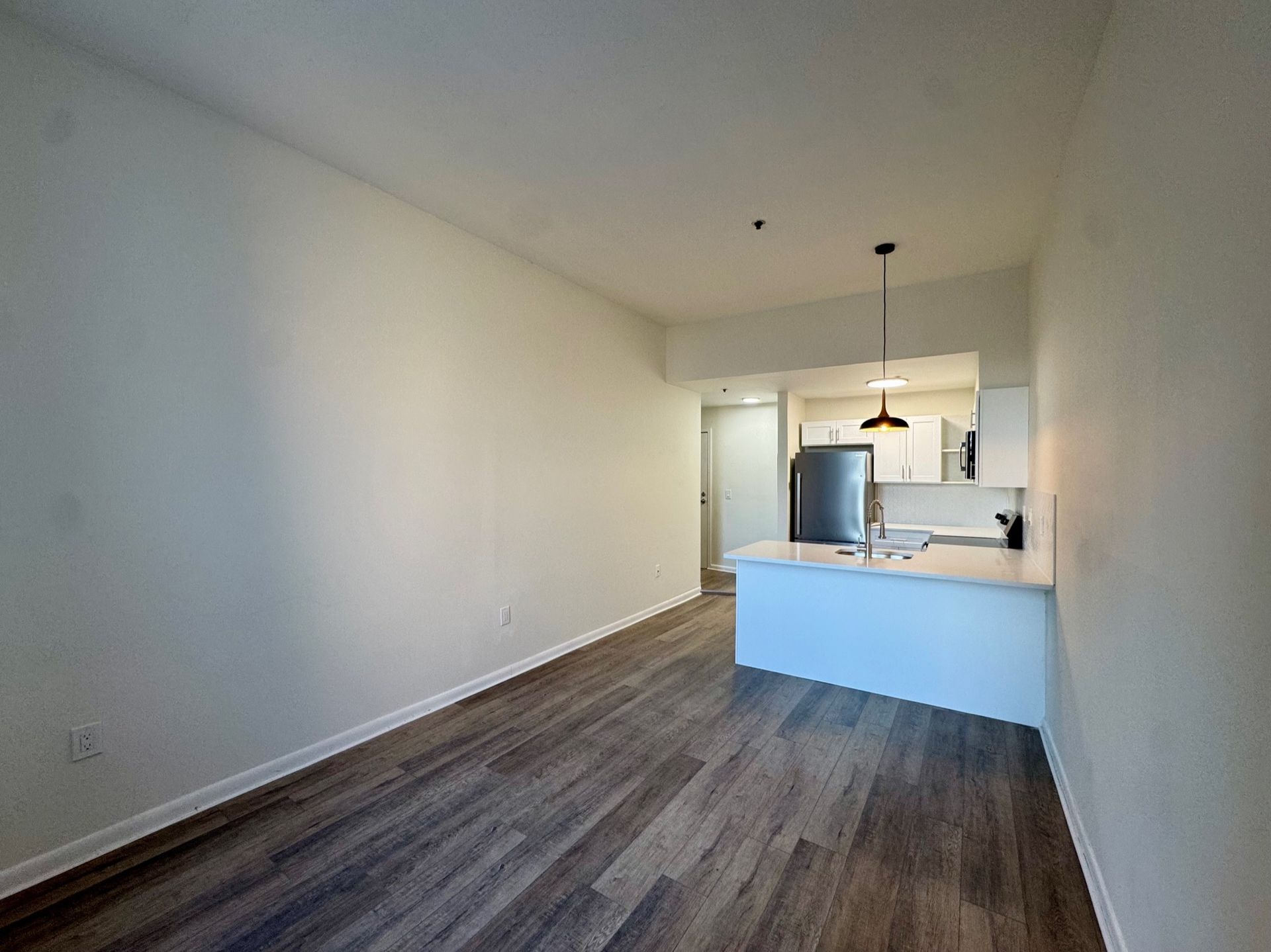 Empty modern kitchen and dining area with white walls, wood floors, and a breakfast bar