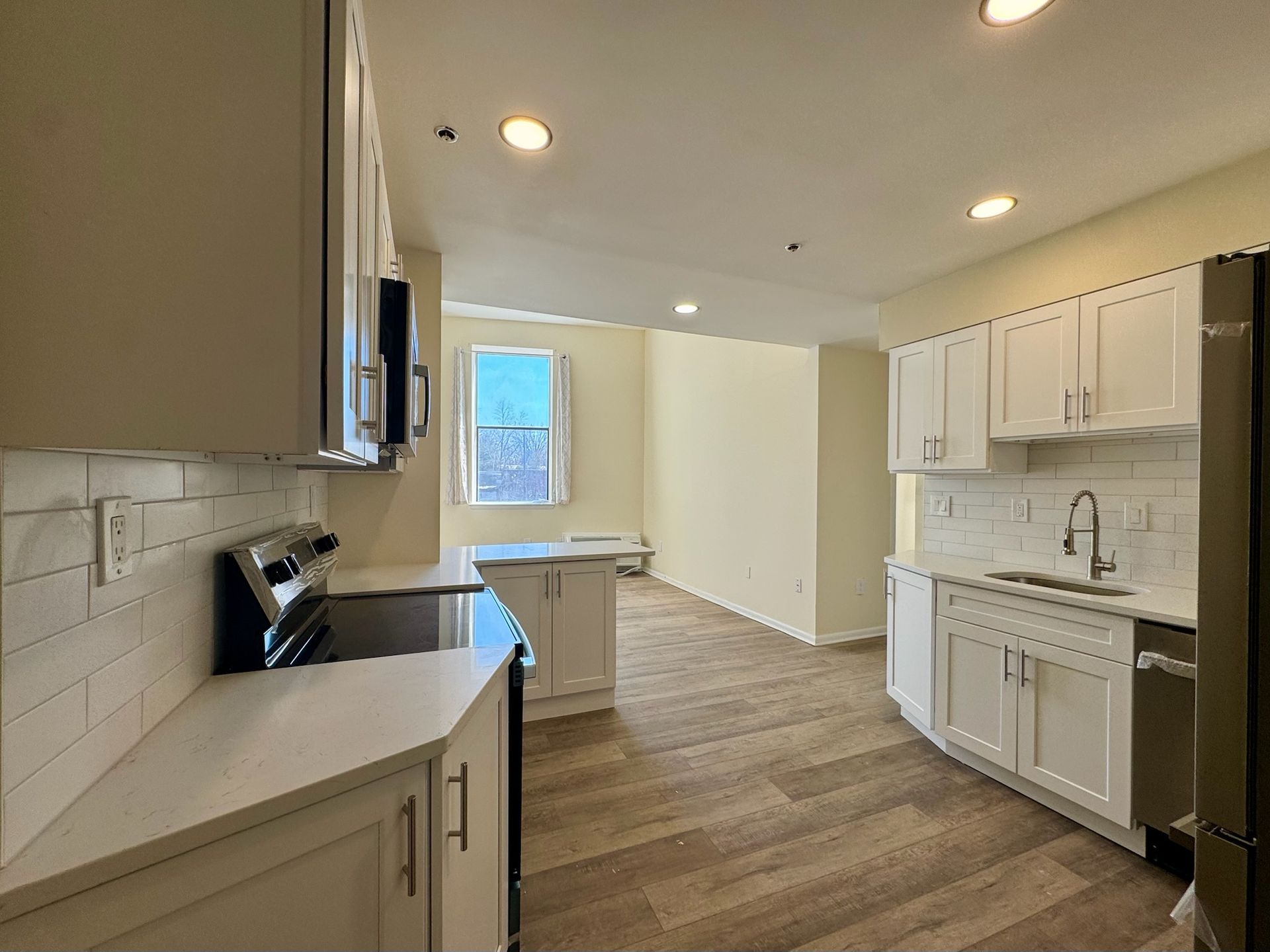 Bright kitchen with white cabinets, black countertops, and wood flooring leading to a small dining area.