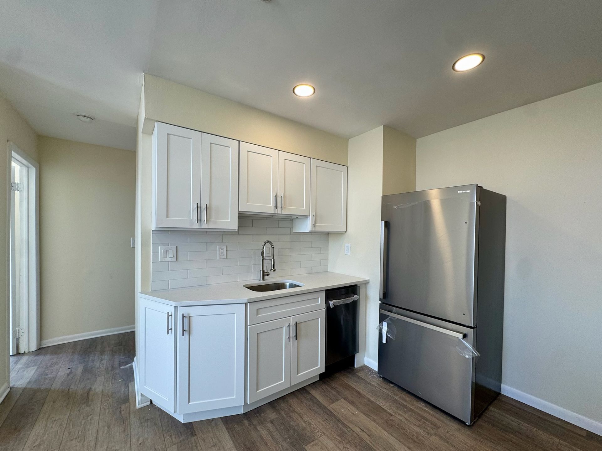 Small modern kitchen with white cabinets, gray countertops, and stainless steel fridge in a bright room