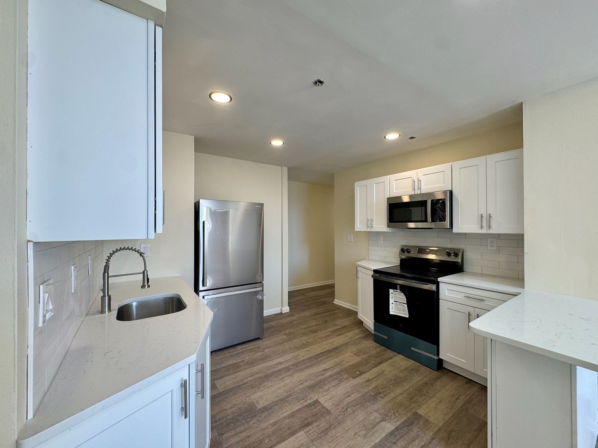 Bright modern kitchen with white cabinets, stainless appliances, and wood-look flooring