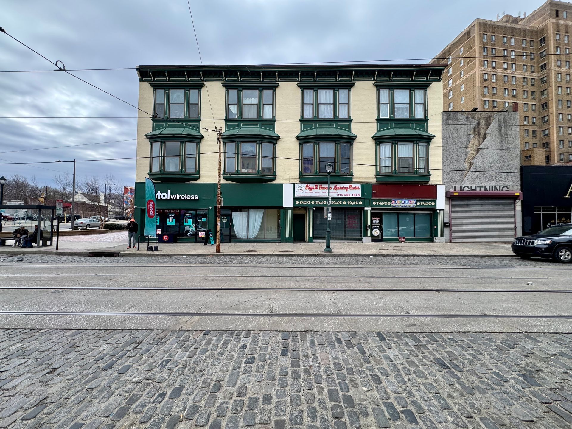 Historic green storefront building across a cobblestone street under an overcast sky
