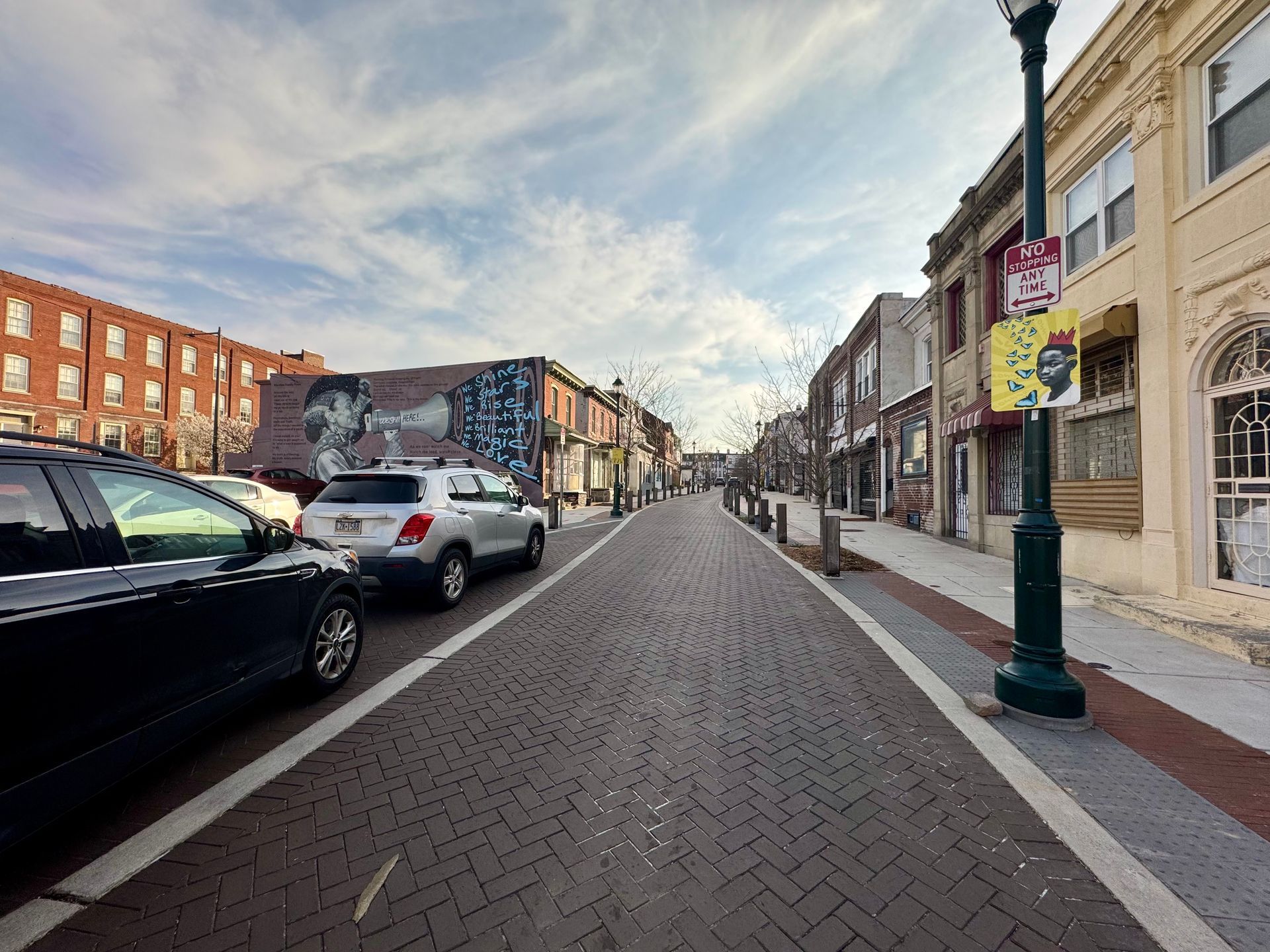 Quiet downtown street with parked cars, brick buildings, and a lamppost under a partly cloudy sky