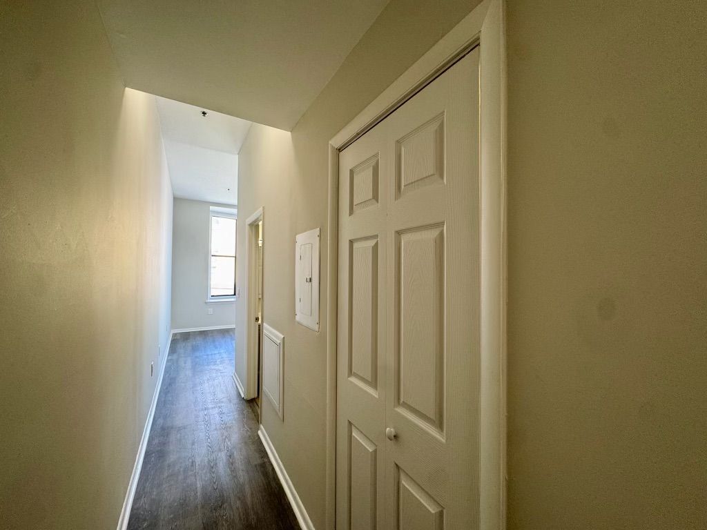 Narrow beige hallway with white doors and a window at the end, leading to a bright room.