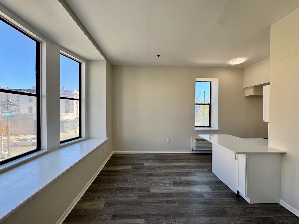 Bright empty room with large windows, gray wood floors, and a small white counter.