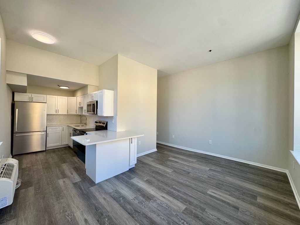 Empty modern apartment with gray wood floors, white kitchen, and open living area.