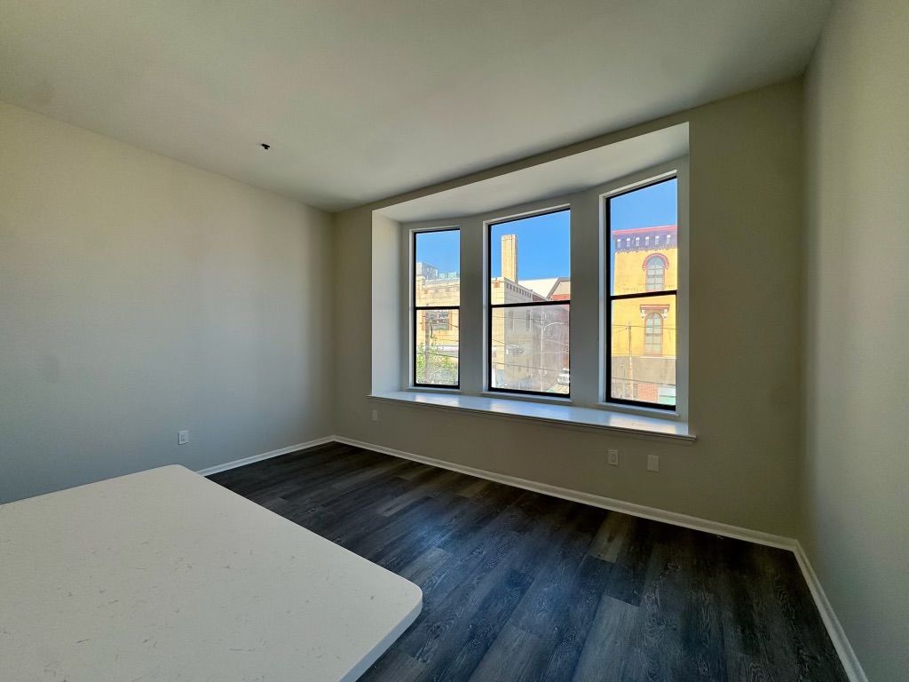 Empty bright bedroom with large bay window and dark wood floor