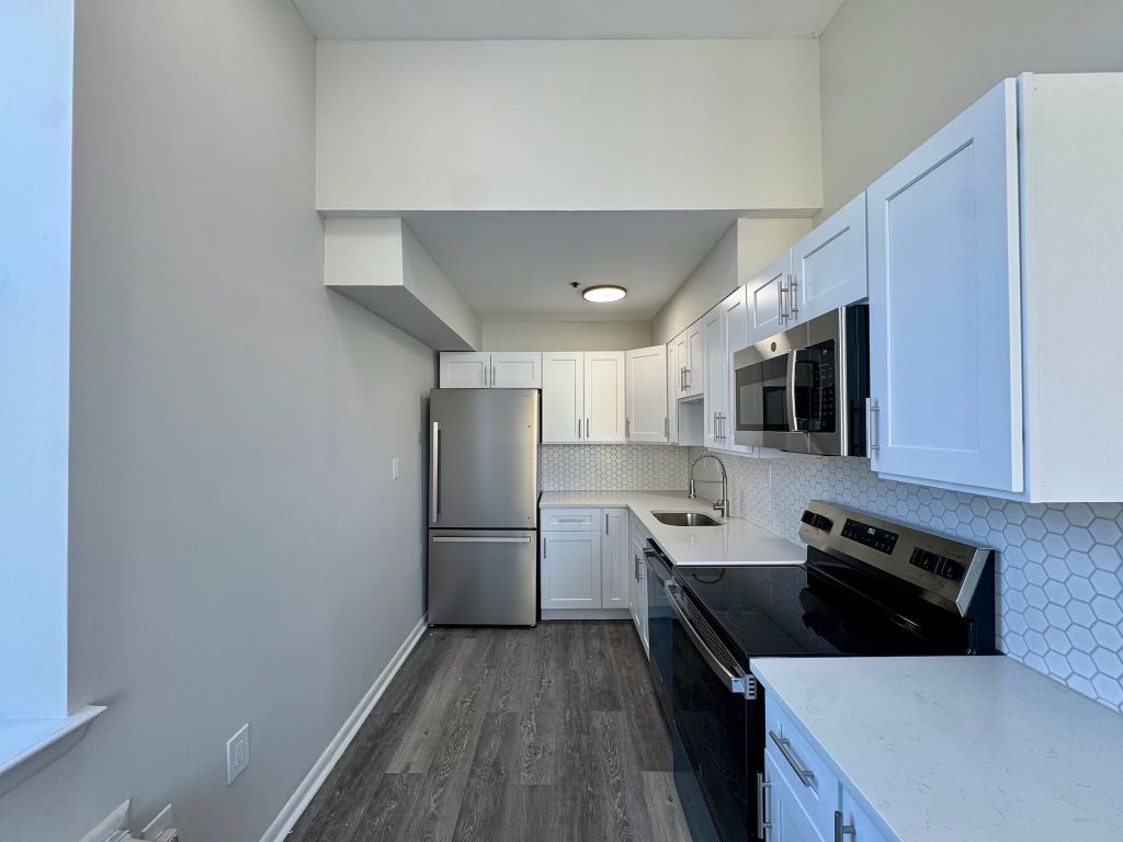 Narrow modern kitchen with white cabinets, stainless appliances, and gray flooring.