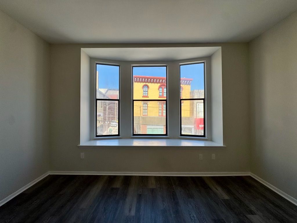 Empty room with dark wood floor and bay window overlooking a brick building.