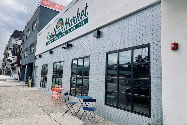 Outdoor storefront with large windows, white brick facade, and small café tables on the sidewalk