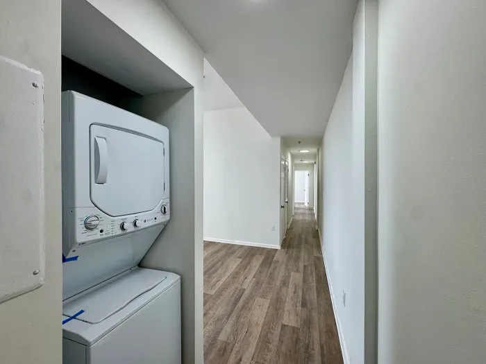 Narrow hallway with white walls, wood floor, and stacked washer-dryer in a recessed closet