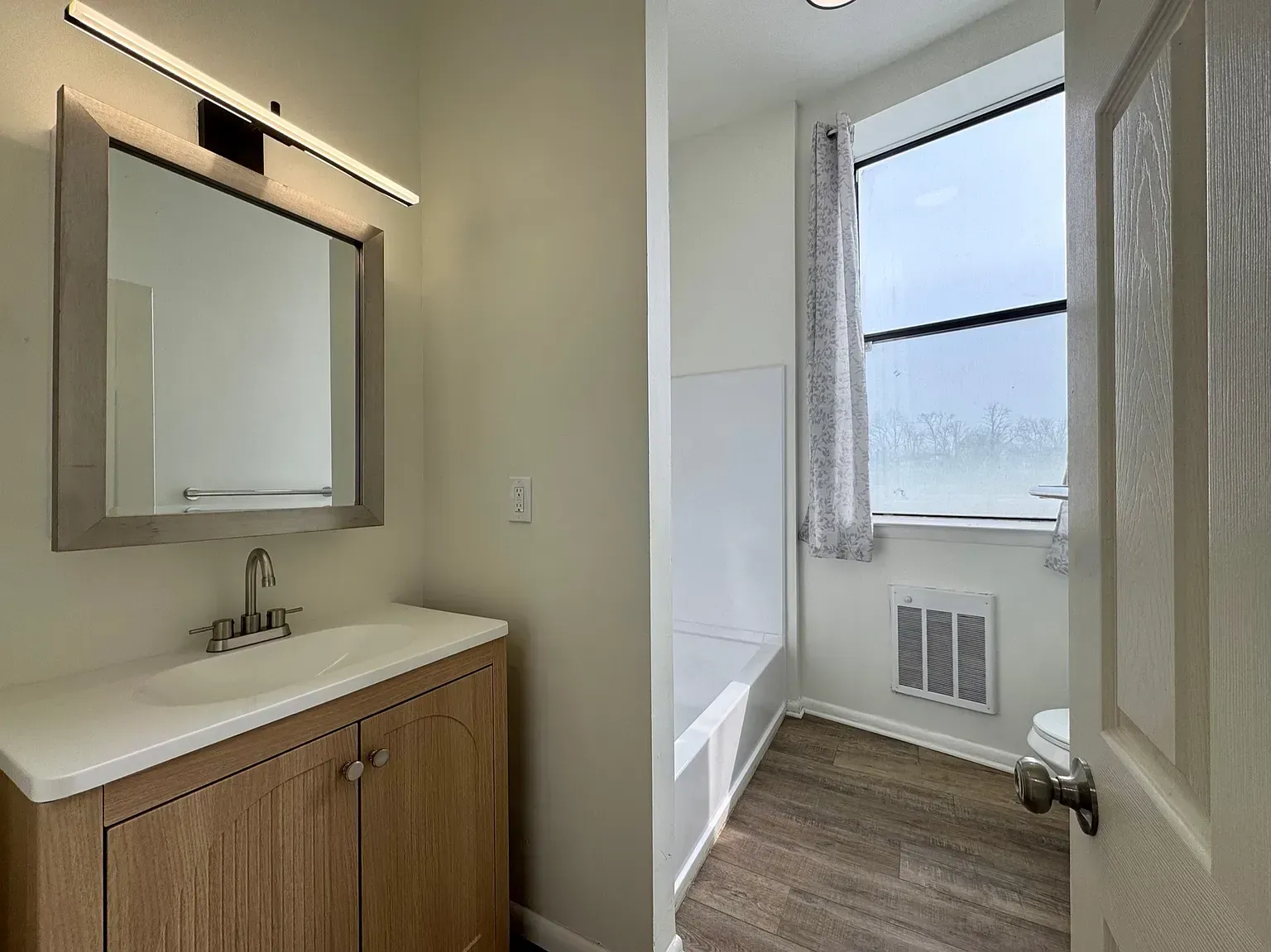Bathroom vanity and separate toilet room with white fixtures, wood cabinet, and window light