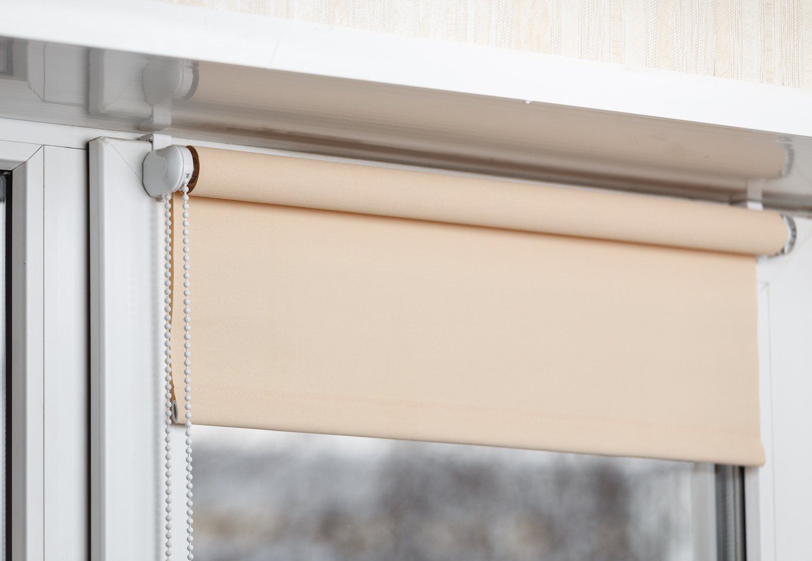 Beige roller blind partially covering a window.