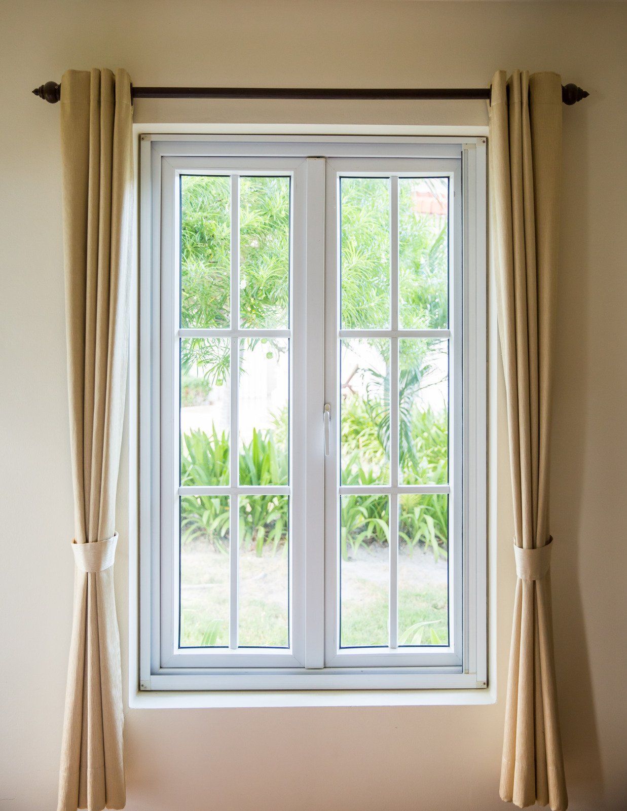 White-framed window with beige curtains, overlooking a green yard.