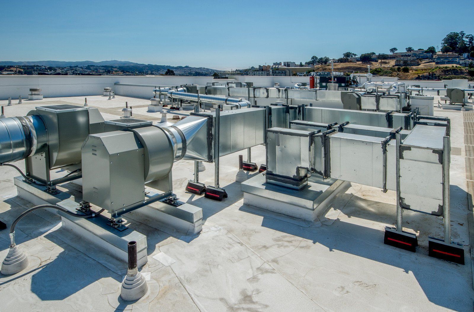 HVAC system on a white rooftop against a blue sky. Silver metal ducts and equipment.