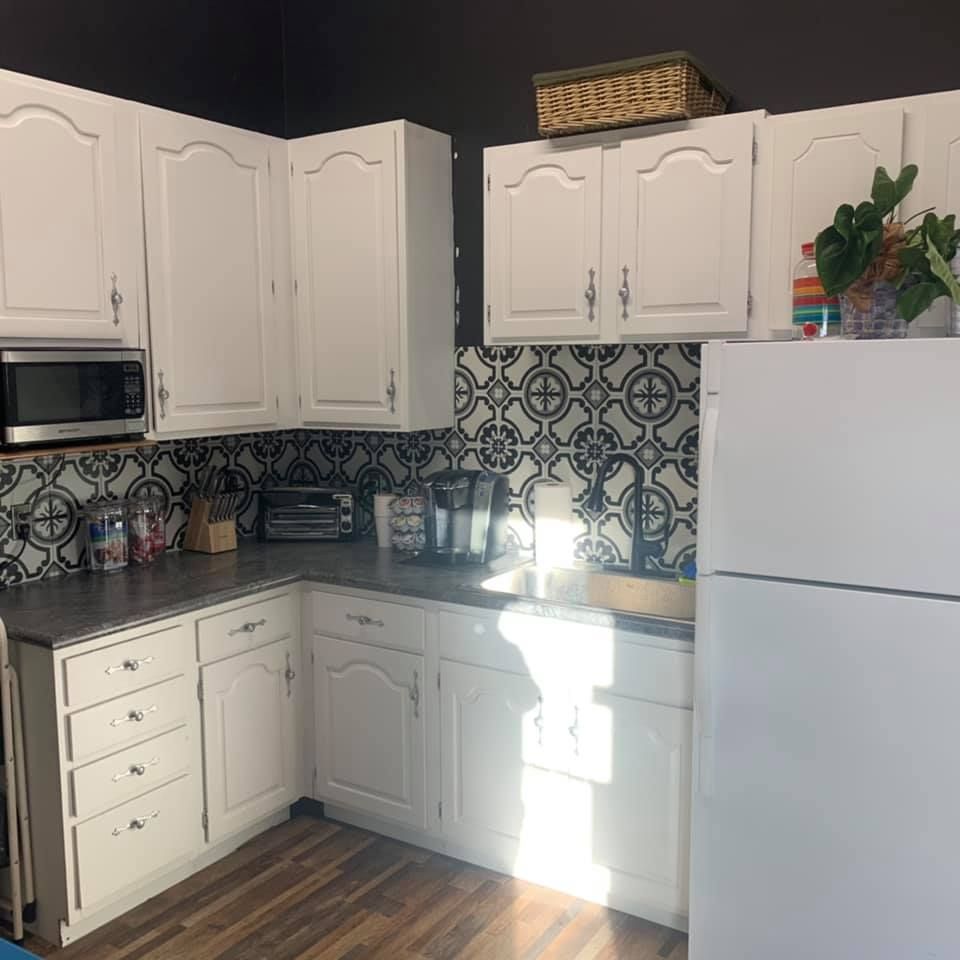 White kitchen cabinets with black and white patterned backsplash, appliances, and wooden floor.