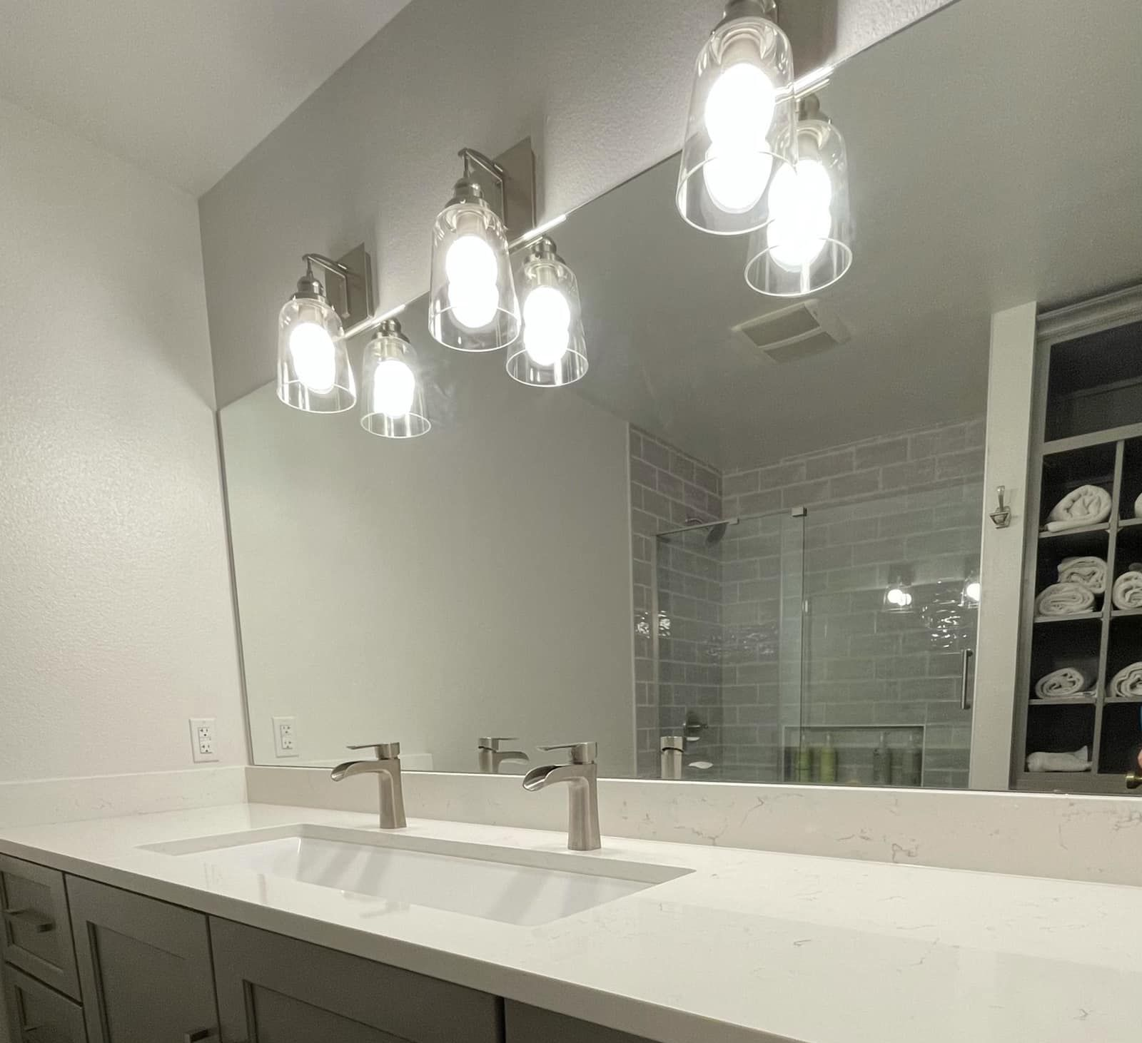 Bathroom with large mirror, double sink, gray cabinets, and modern light fixtures.