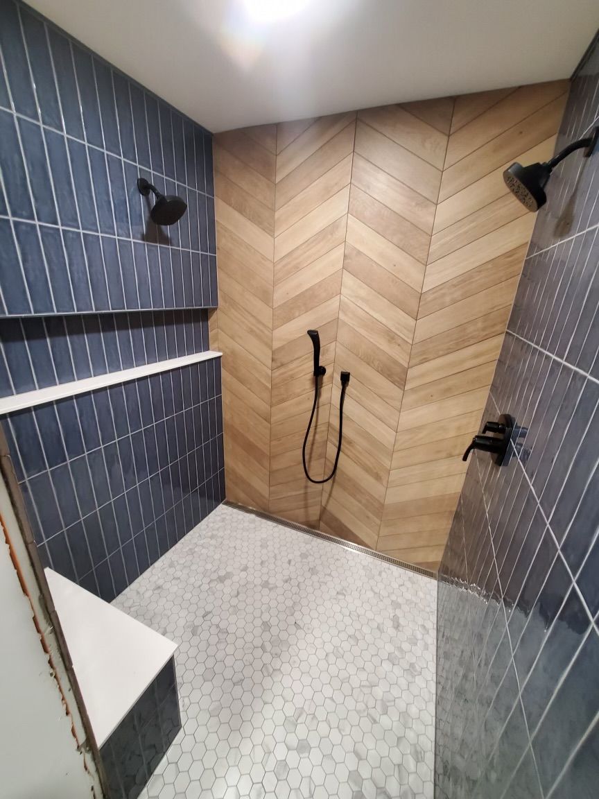 A modern shower with blue tile walls, wooden chevron accent, and black fixtures.