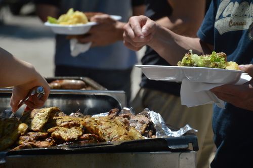 A group of people are standing around a grill eating food.