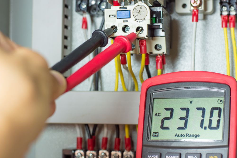 A person uses a multimeter to measure voltage on electrical wiring in a panel, with a reading of 237 volts.