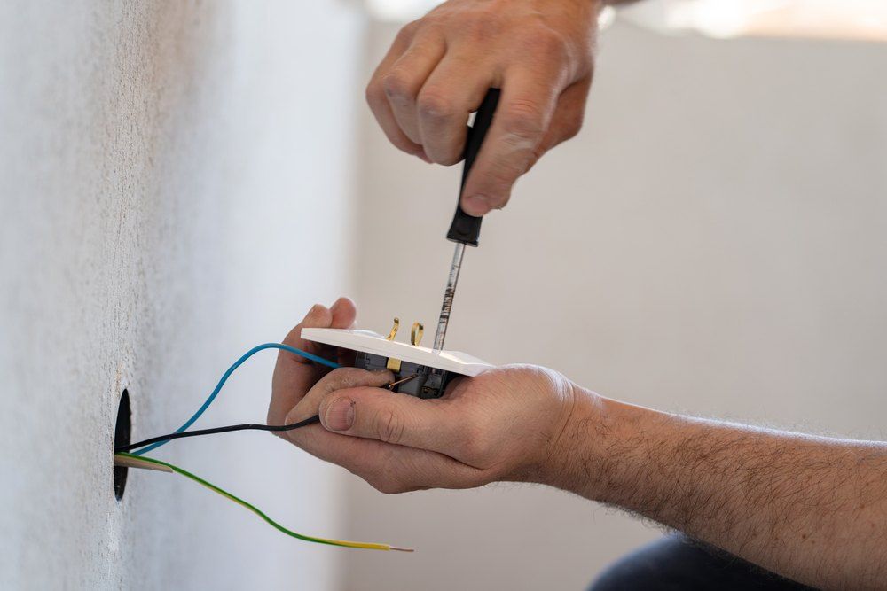 Person installing an electrical outlet, using a screwdriver on the wires.
