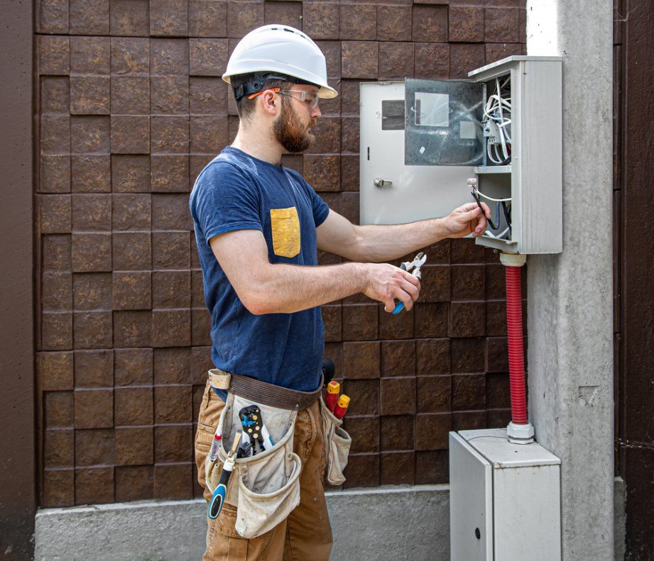 Electrician in a hard hat working on an electrical box outdoors, using pliers.
