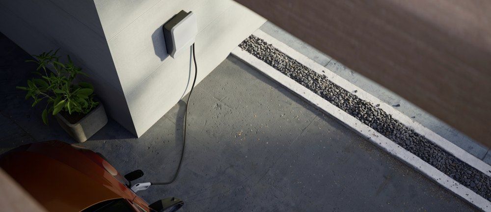 A modern electric vehicle charging near a house with a planter and gravel drainage.