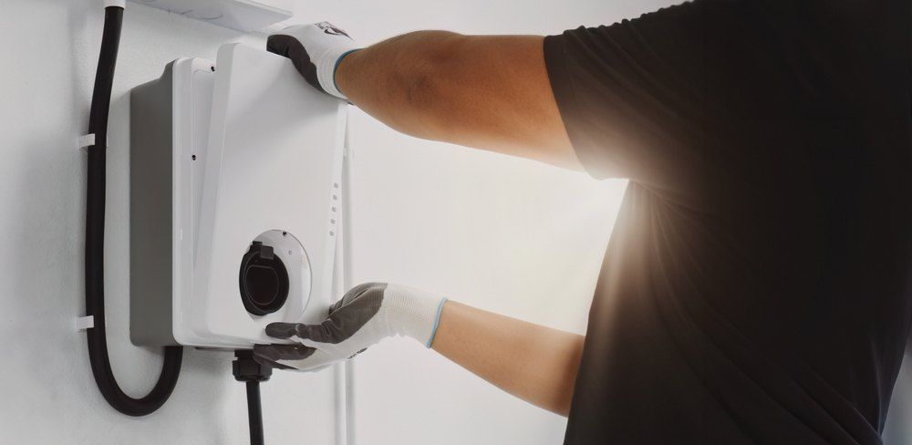 A person wearing gloves installing a white wall-mounted charging station.